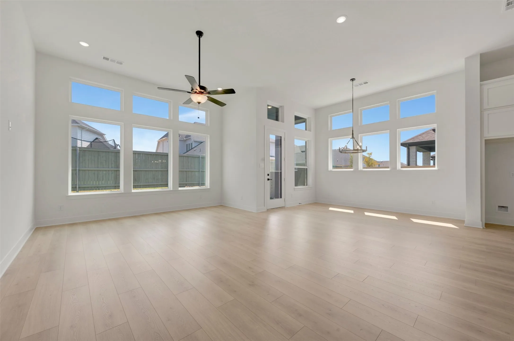 Spacious room featuring high ceilings, light wood-finish flooring, abundant natural light from multiple large windows, and recessed lighting