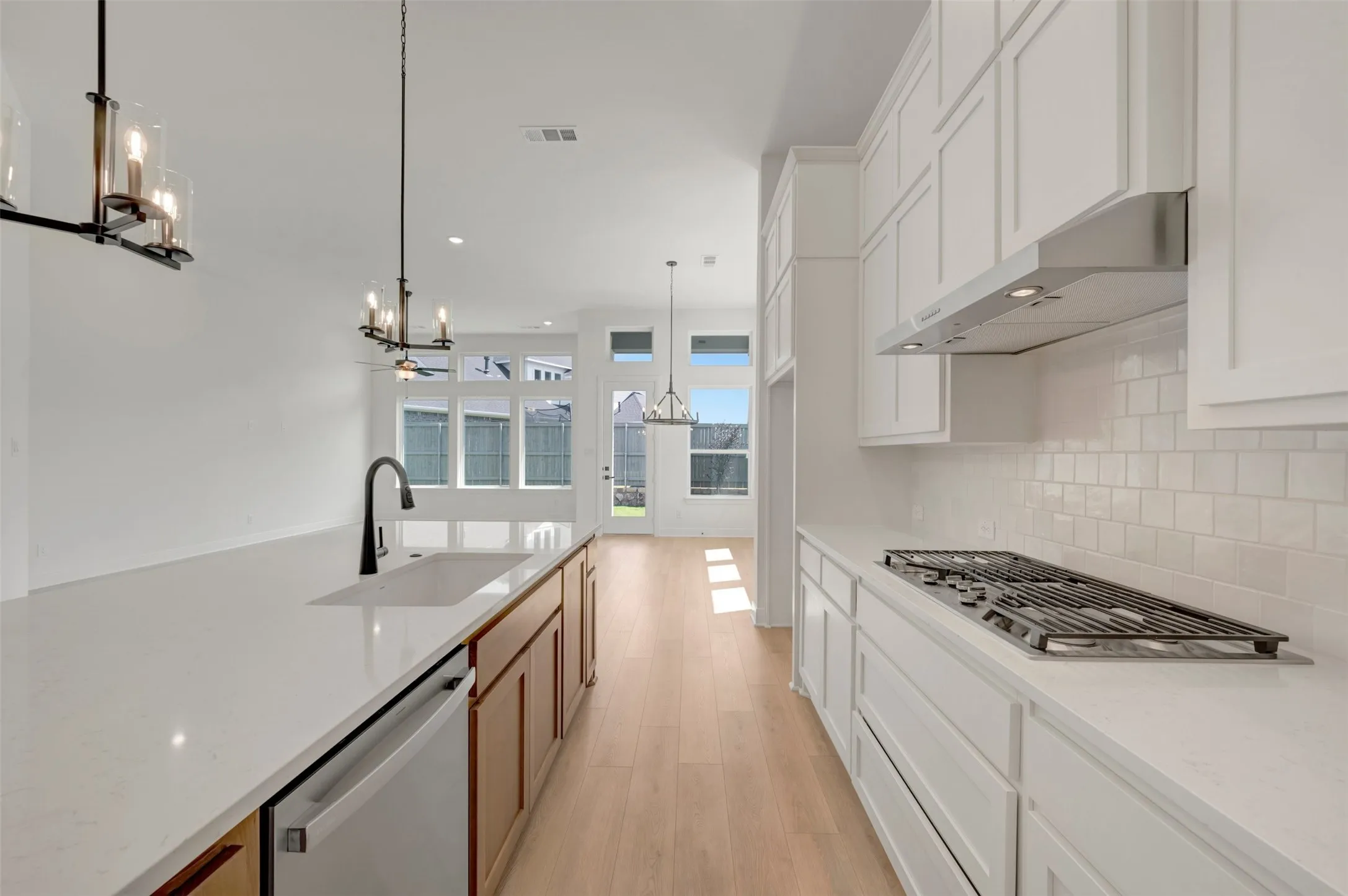 Contemporary kitchen featuring an expansive island with an undermount sink and matte black faucet, light wood-finish flooring, white shaker cabinetry, a gas cooktop, and a subway tile backsplash