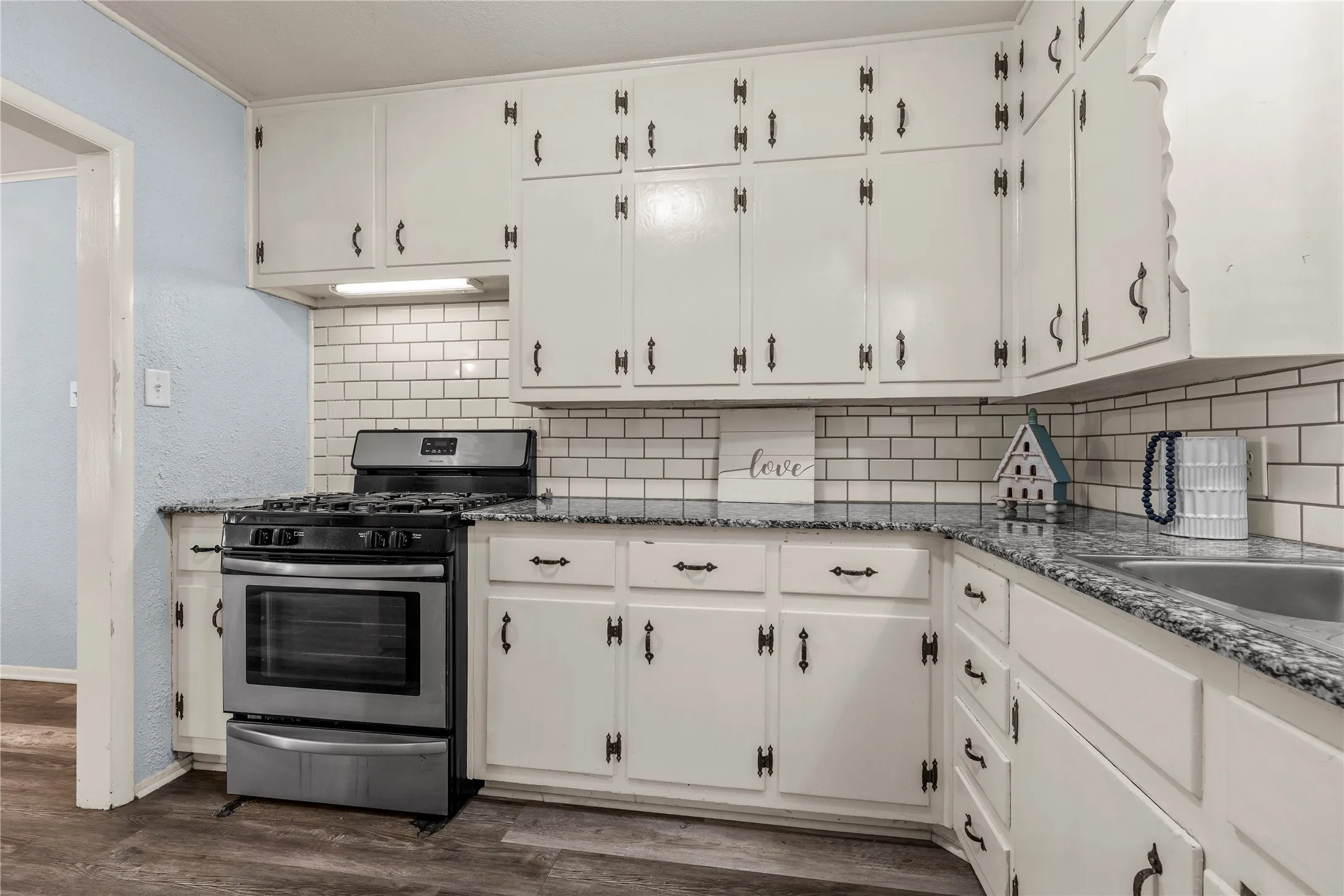 Kitchen featuring stainless steel gas range, dark stone counters, and white cabinets