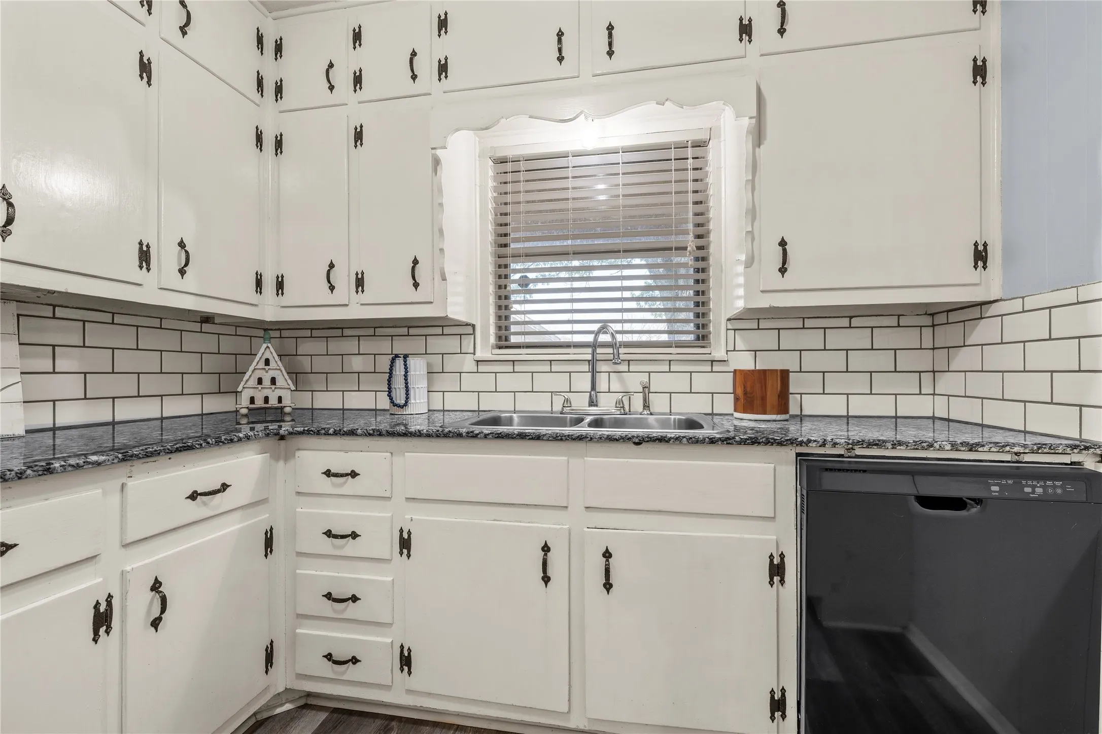 Kitchen with dishwasher, white cabinets, dark stone countertops, and decorative backsplash