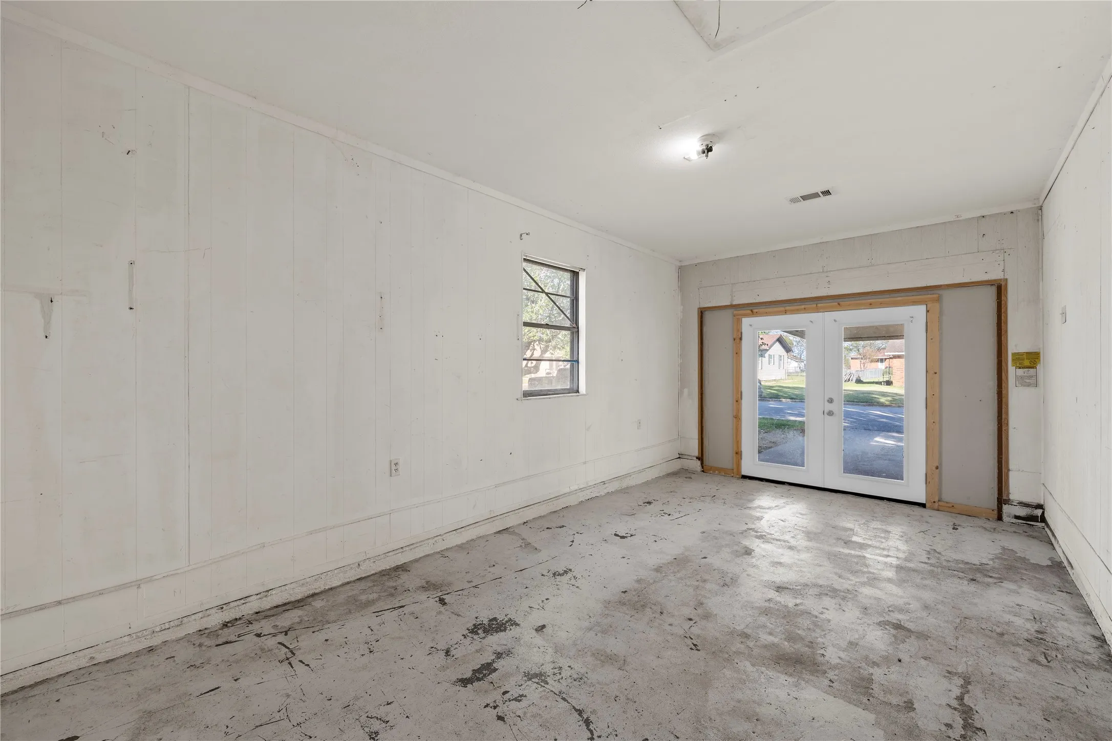 Spare room with french doors, concrete flooring, and wooden walls