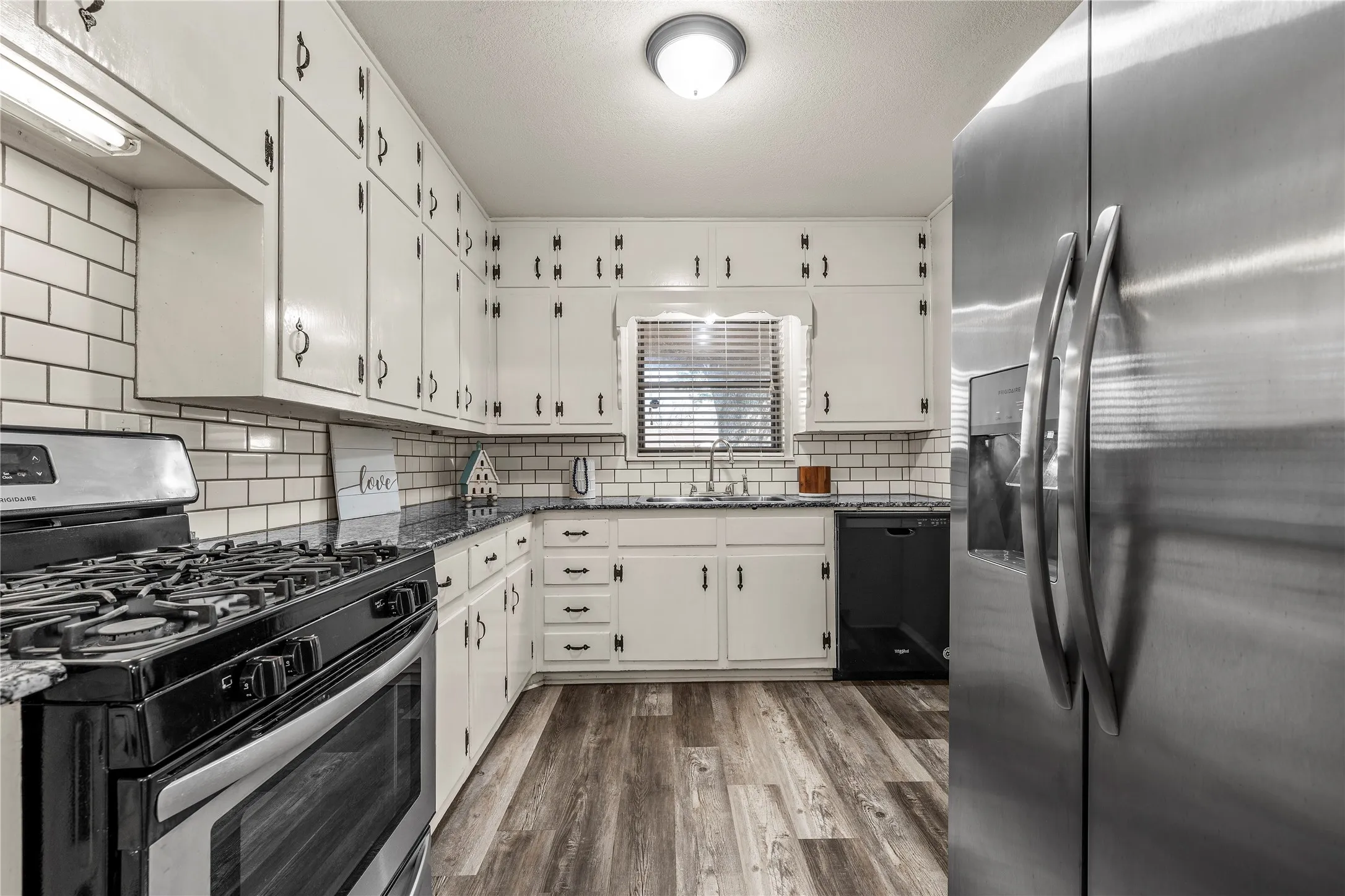 Kitchen featuring stainless steel appliances, dark stone counters, dark wood finished floors, and white cabinets