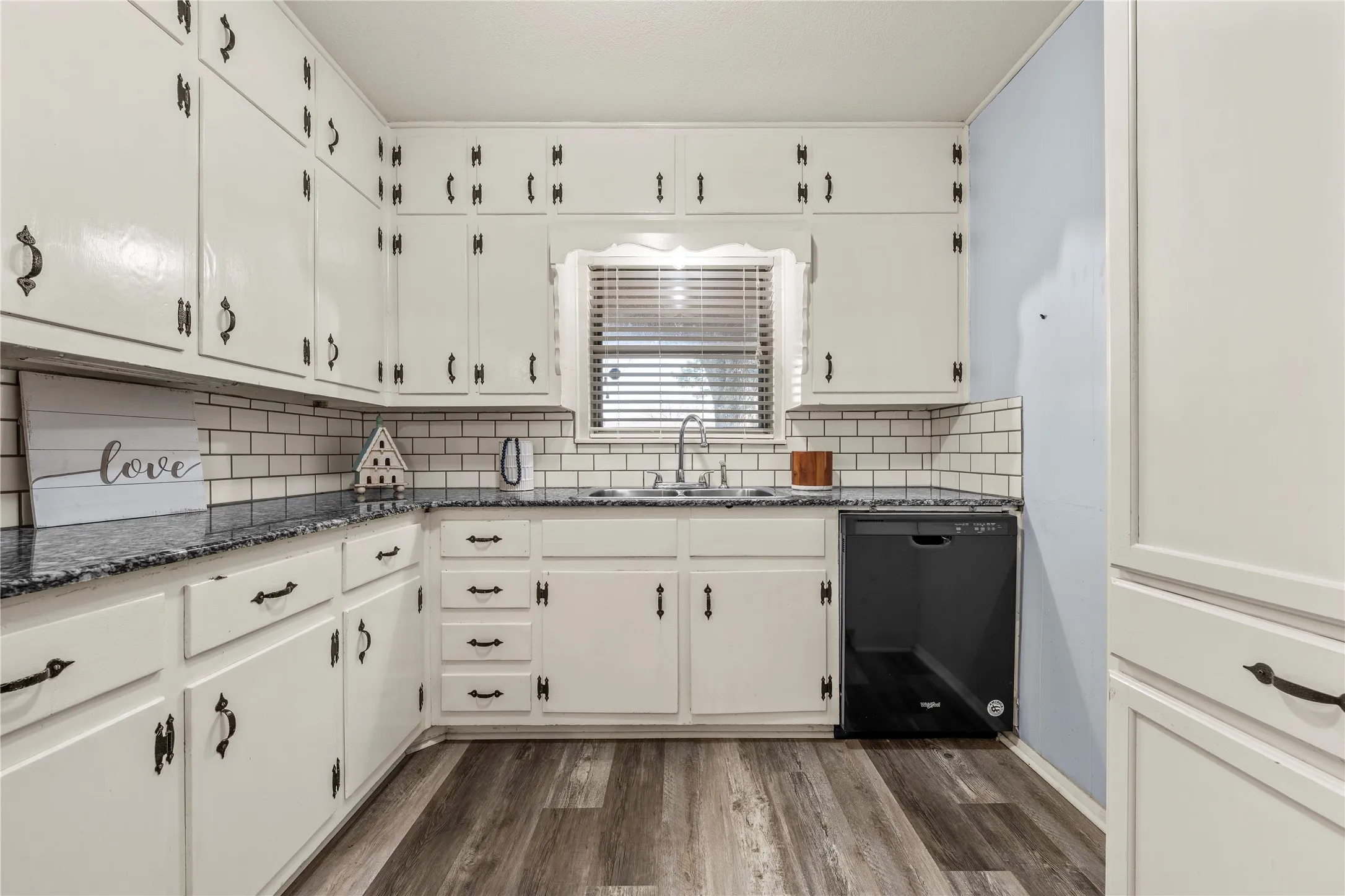 Kitchen with black dishwasher, dark stone counters, white cabinetry, and dark wood finished floors