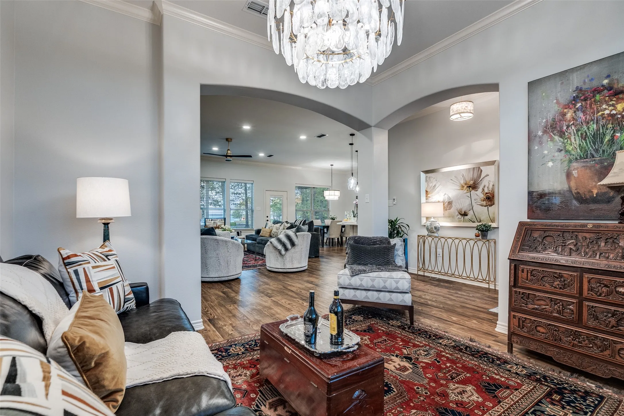 Living room featuring arched walkways, suspended lighting, ornamental molding, dark wood-type flooring, and ceiling fan