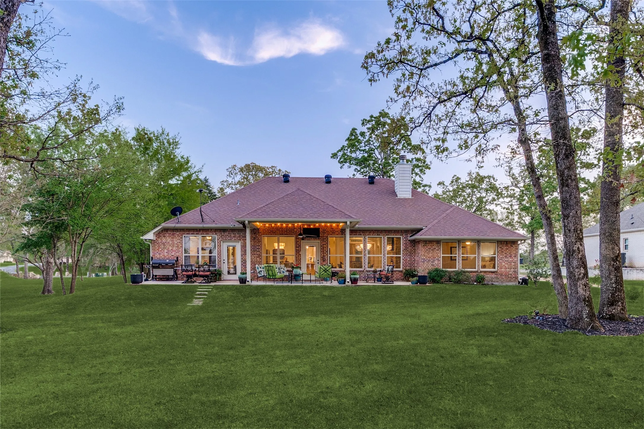 Back of property featuring a lawn, a chimney, brick siding, and a patio area
