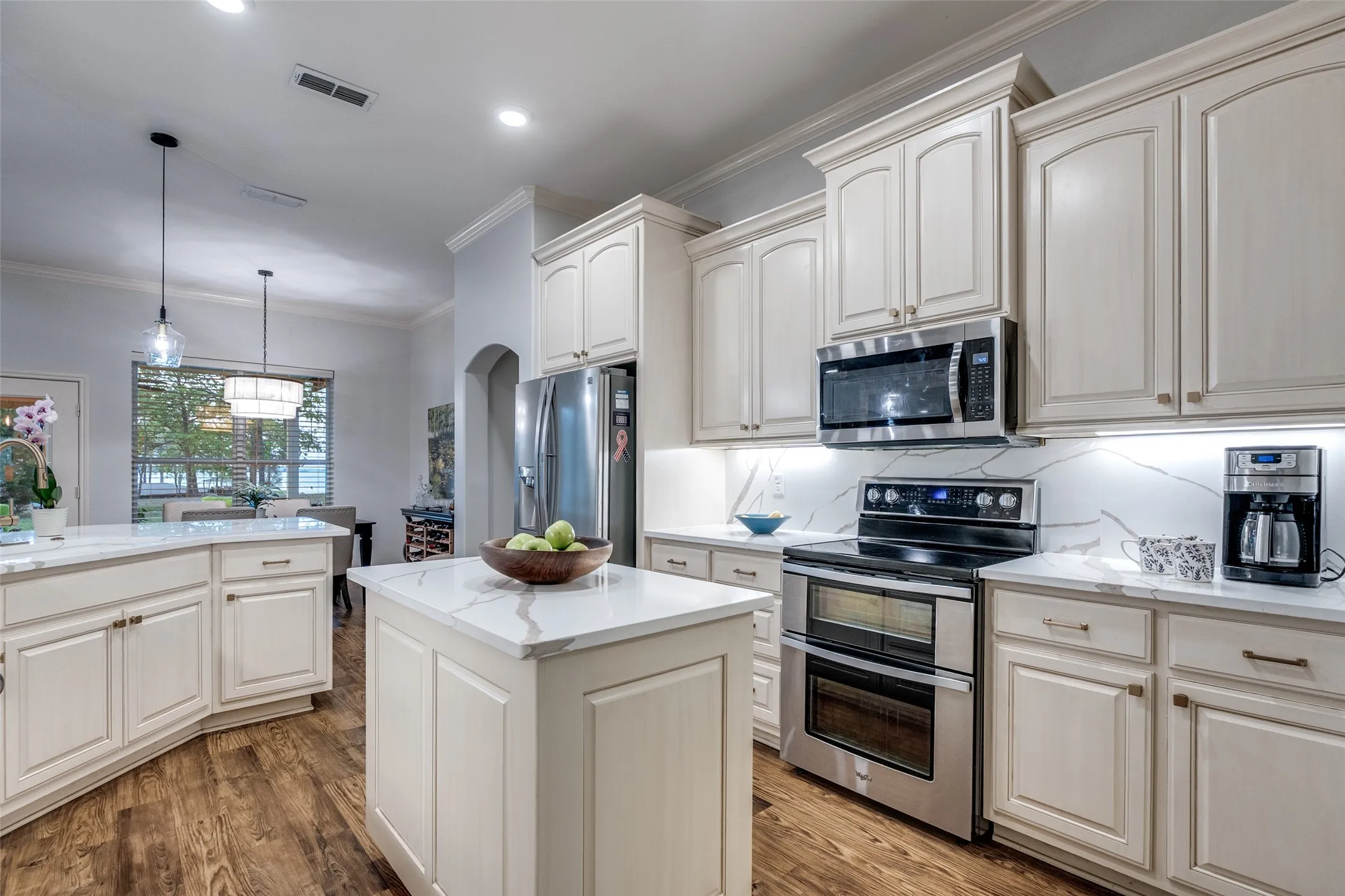 Kitchen with stainless steel appliances, light stone countertops, a kitchen island, backsplash, and dark wood-style flooring