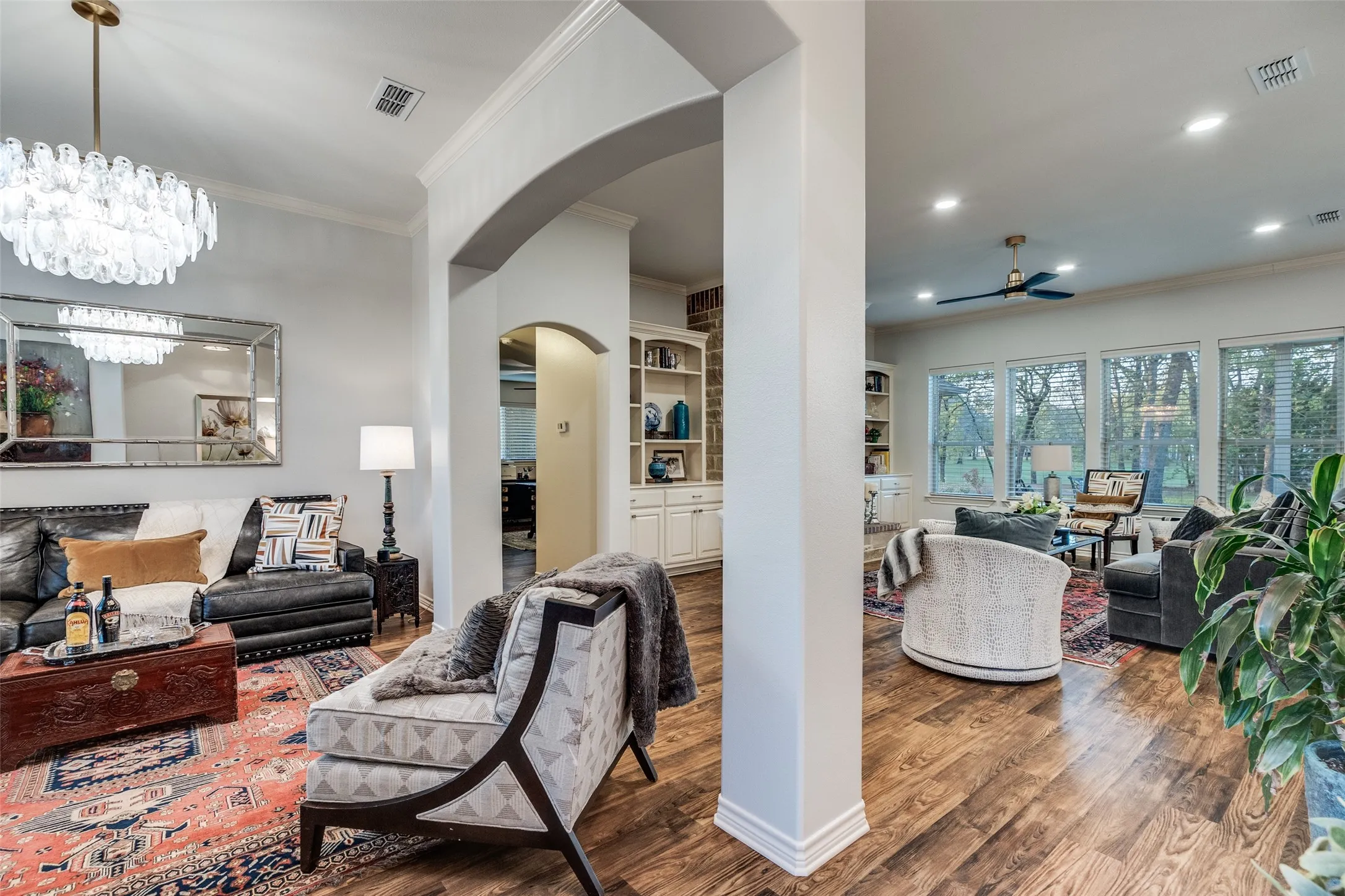 Living room with ornamental molding, dark wood-style flooring, suspended lighting, arched walkways, and built in shelves