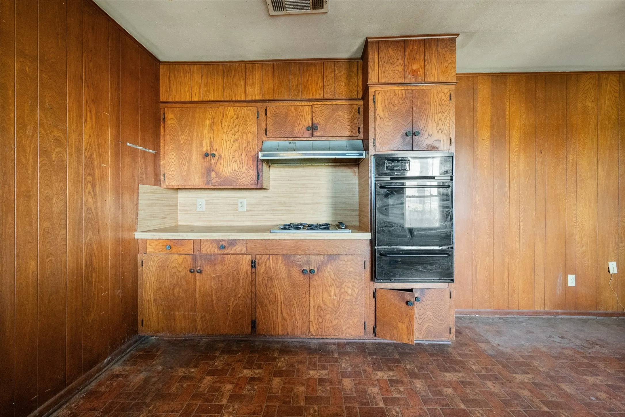 Kitchen featuring wooden walls, light countertops, black oven, a warming drawer, and wood cabinets
