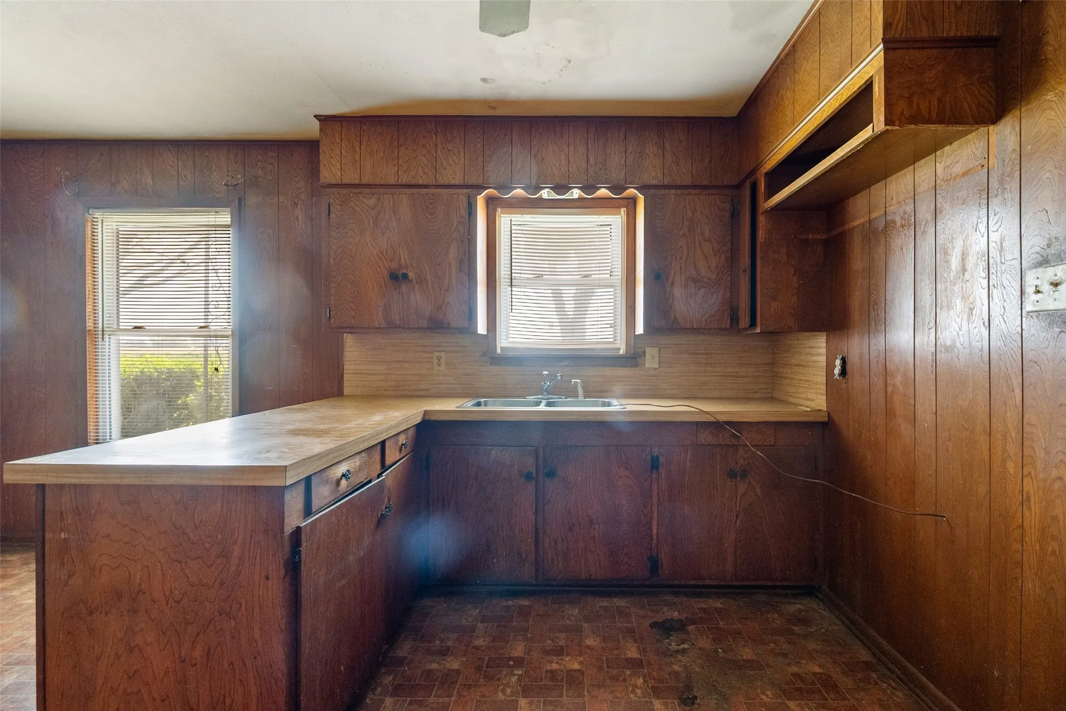Kitchen with a peninsula, light countertops, paneling, brick patterned floors, and healthy amount of natural light