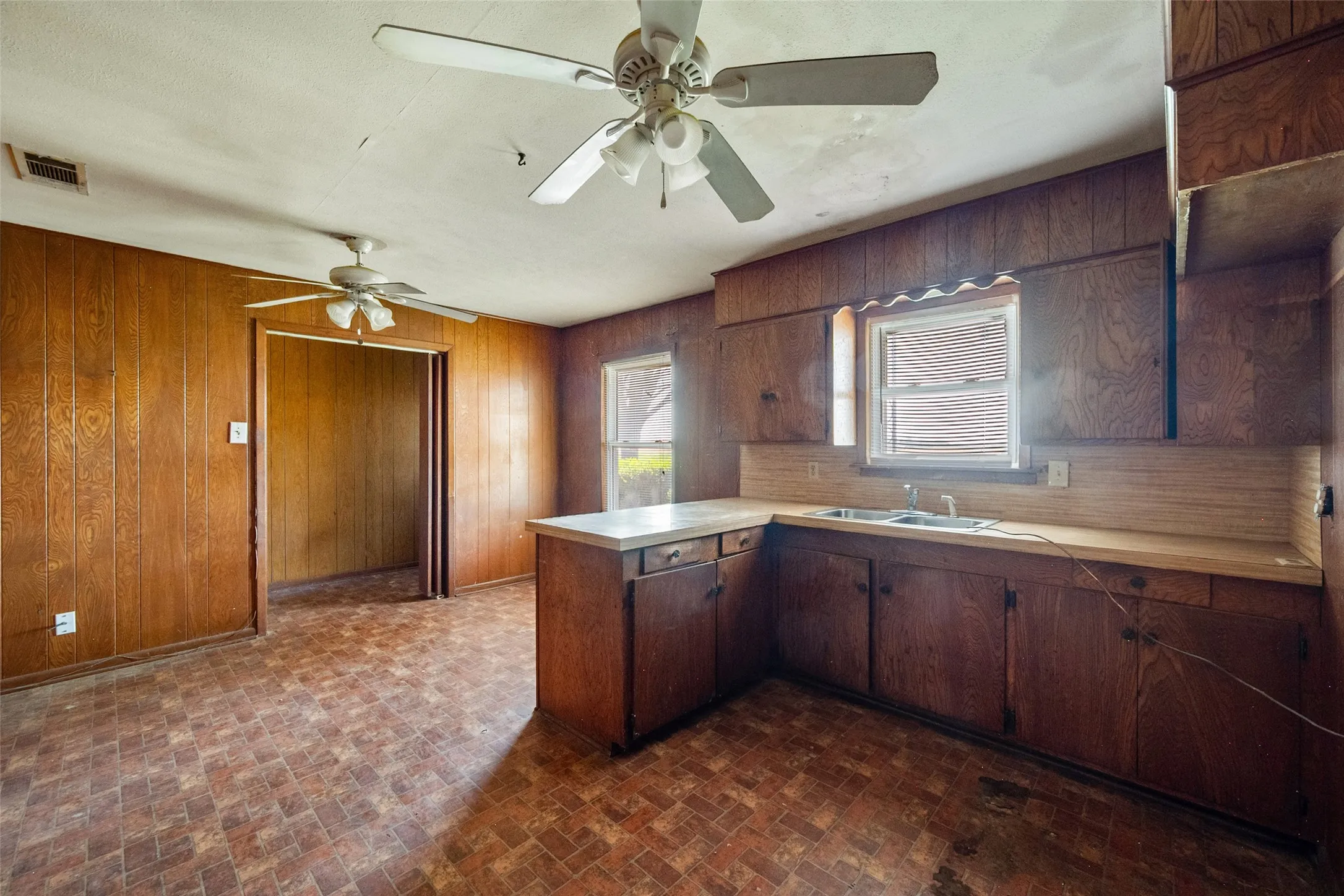 Kitchen with a peninsula, light countertops, brick patterned flooring, paneling, and a ceiling fan