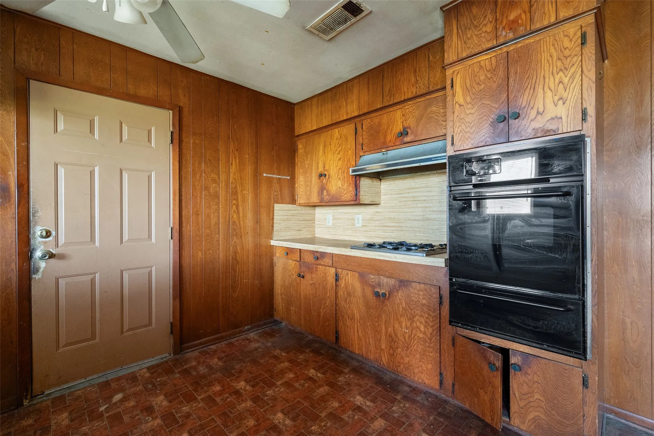 Kitchen with wood cabinetry, light countertops, oven, a warming drawer, and brick patterned flooring