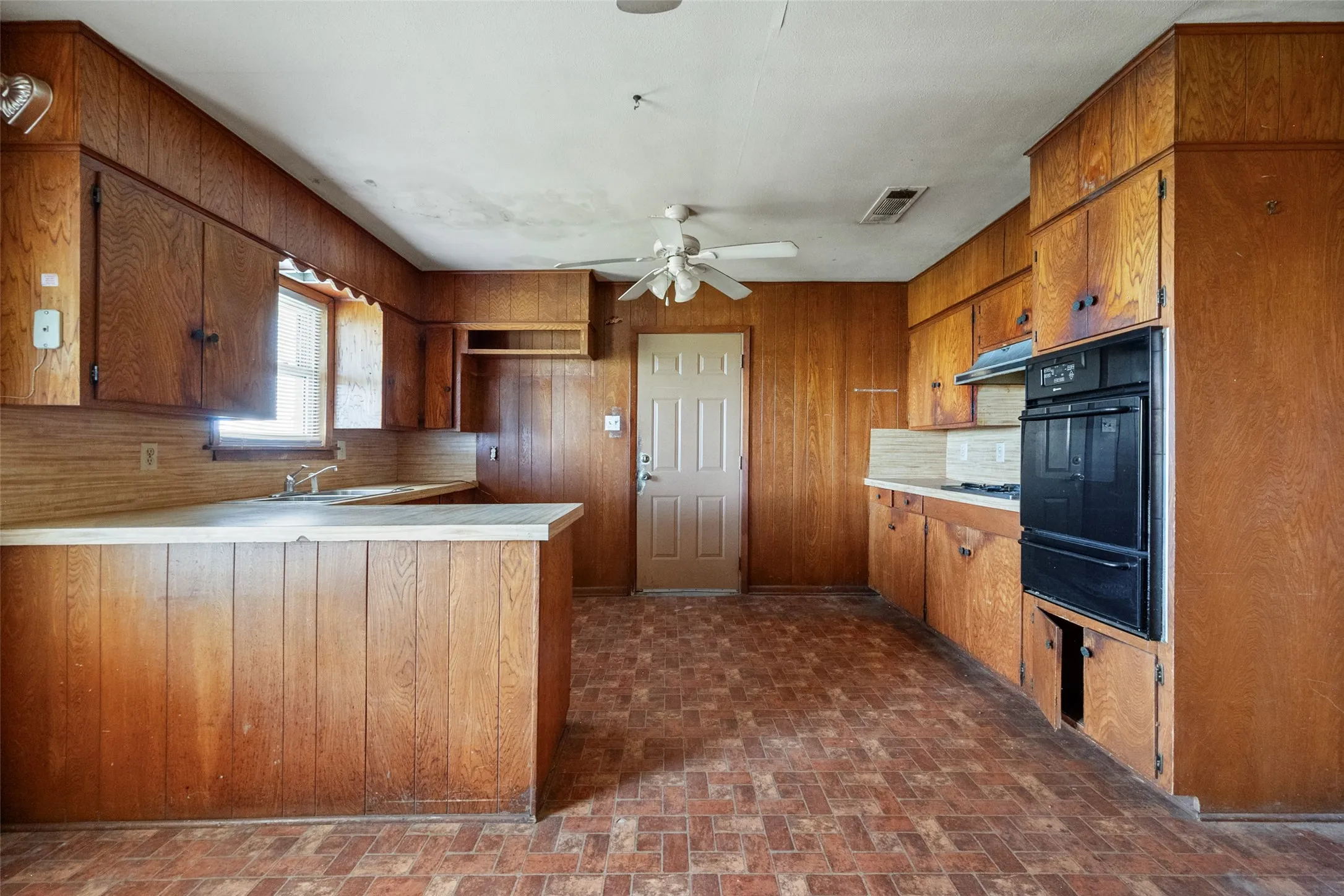 Kitchen with wood cabinetry, brick patterned floors, light countertops and a peninsula