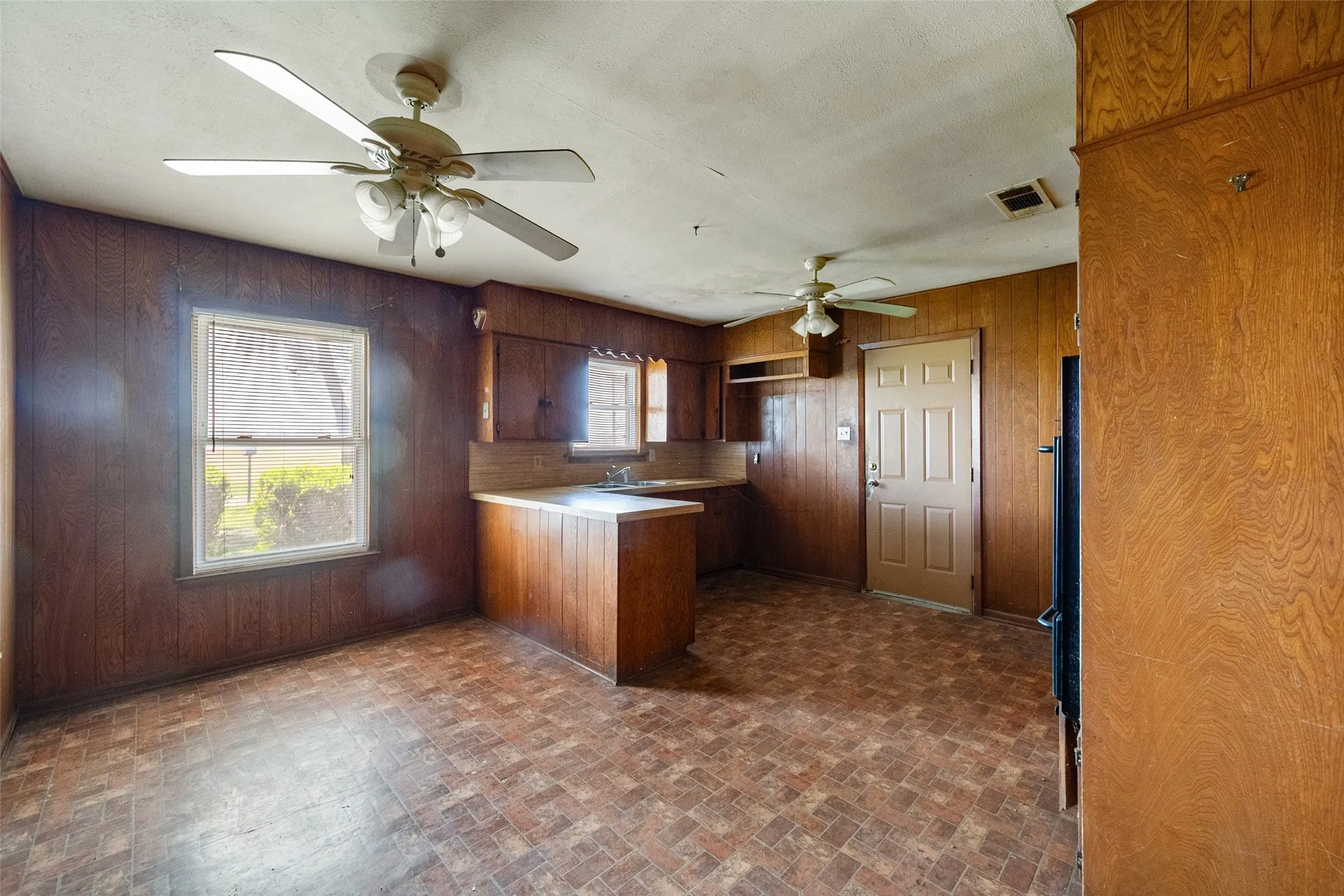 Kitchen with a peninsula, brick patterned floors, light countertops, and paneling