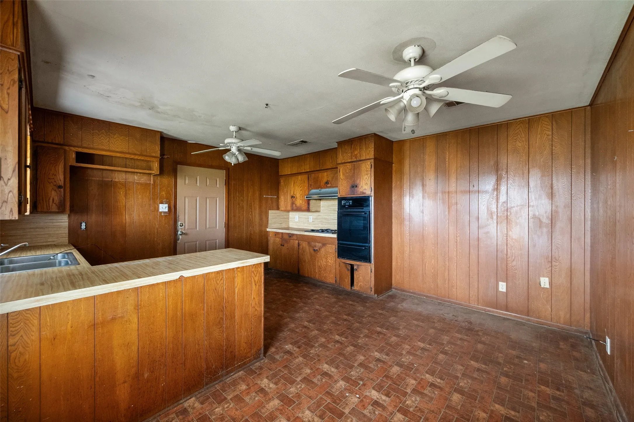 Kitchen with wood cabinets, a peninsula, light countertops, and paneling