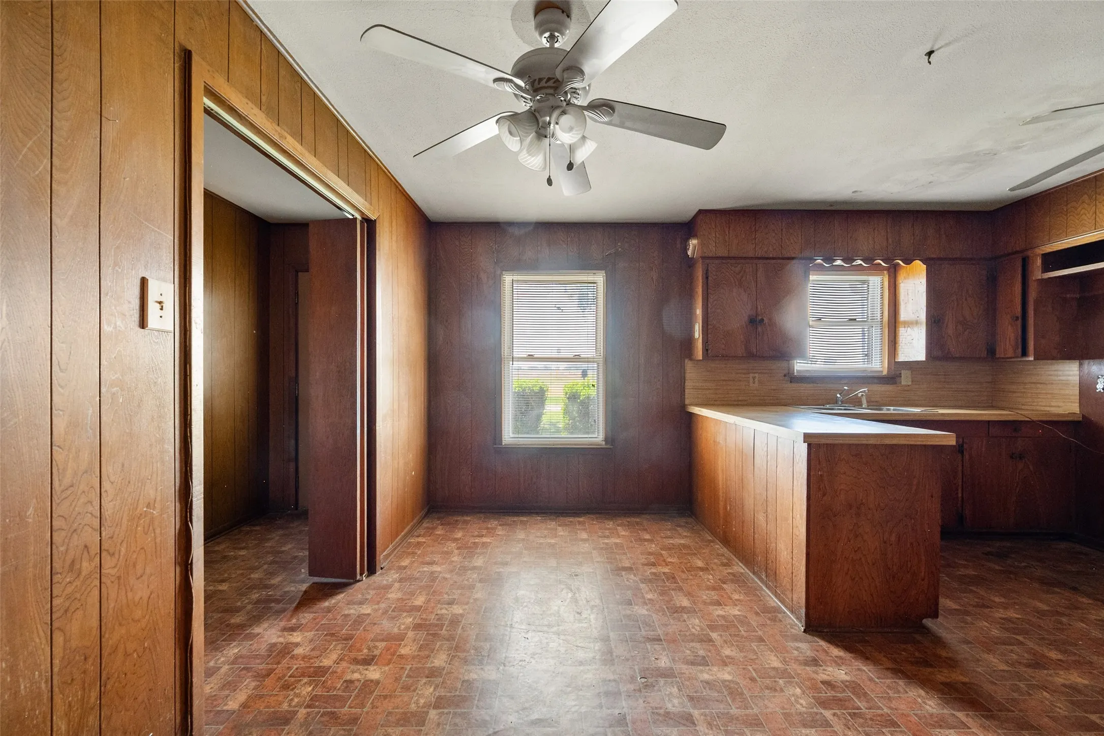 Kitchen featuring a peninsula, light countertops, paneling, and brick patterned floors