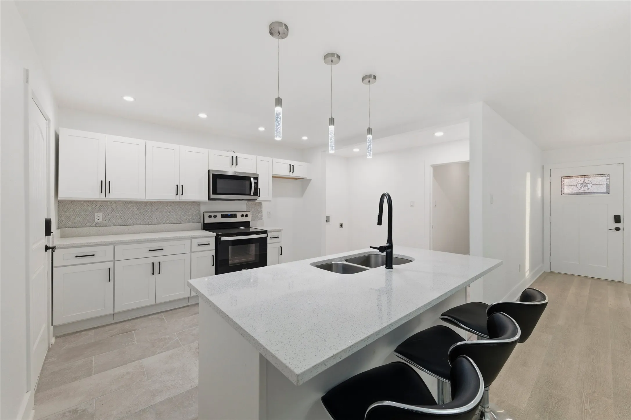 Kitchen featuring stainless steel appliances, a breakfast bar, white cabinets, light stone counters, and hanging light fixtures