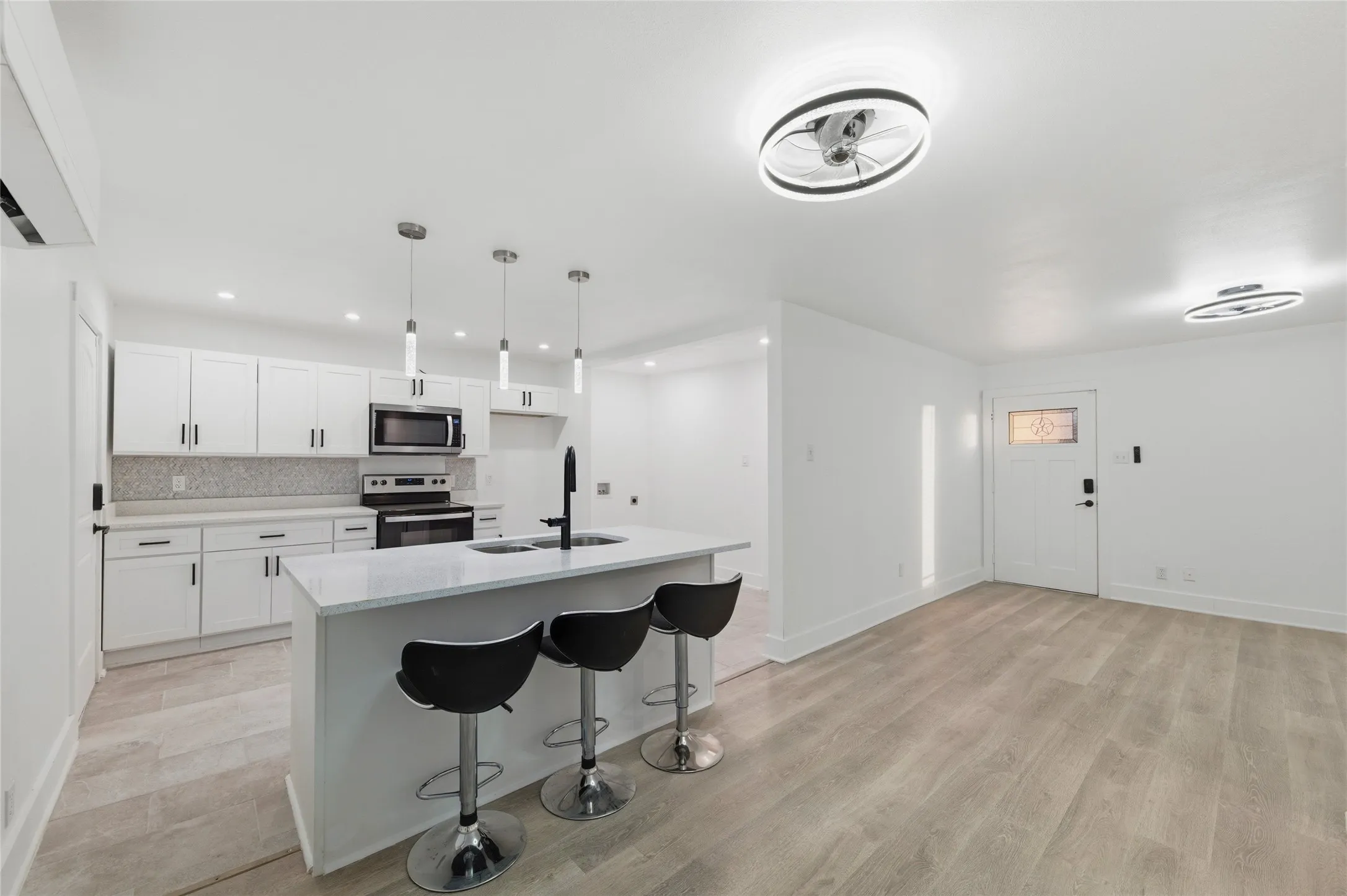 Kitchen featuring white cabinets, stainless steel appliances, a breakfast bar area, a kitchen island with sink, and light wood-type flooring