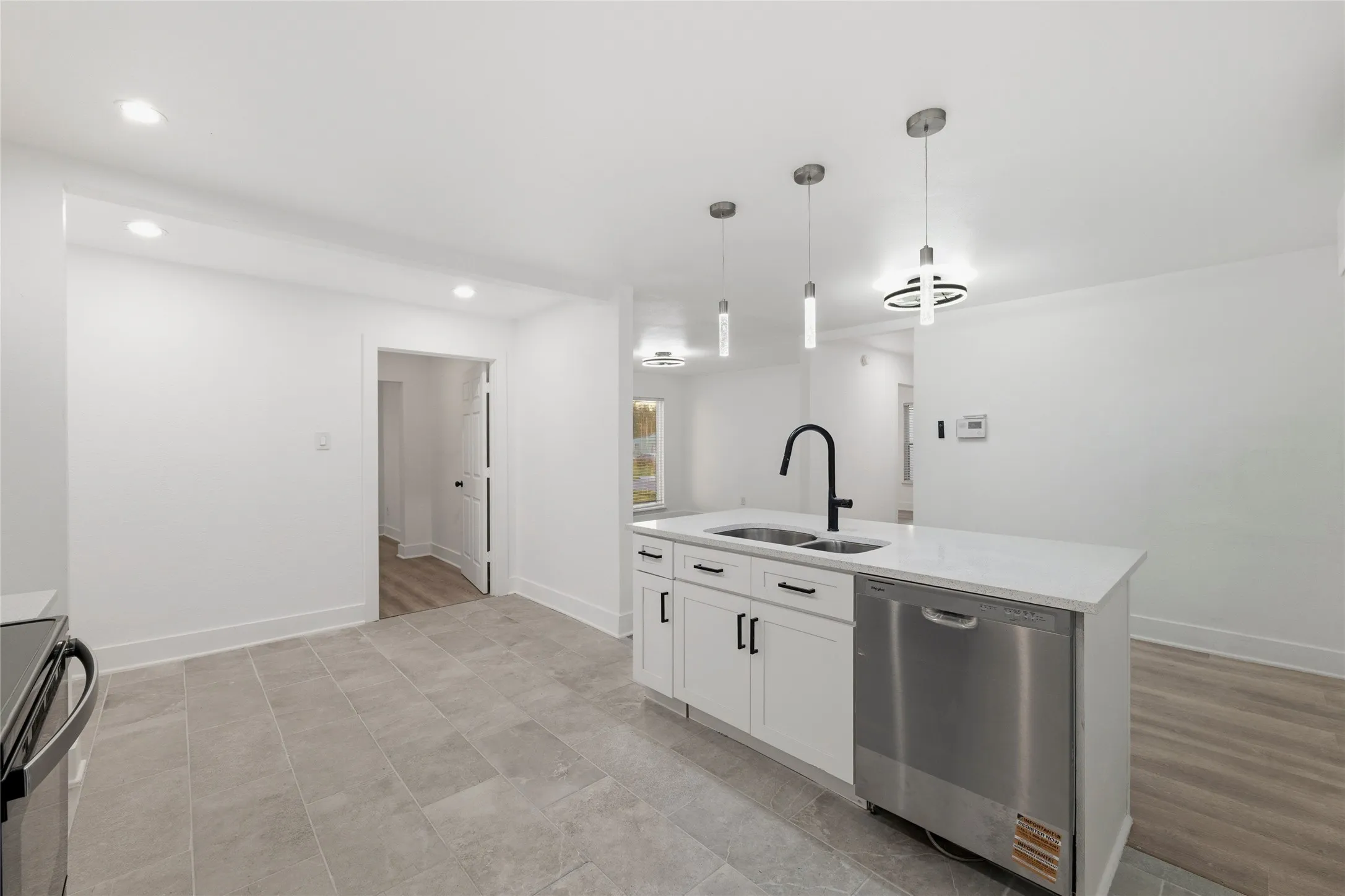 Kitchen featuring stainless steel appliances, a kitchen island with sink, white cabinets, decorative light fixtures, and light stone countertops