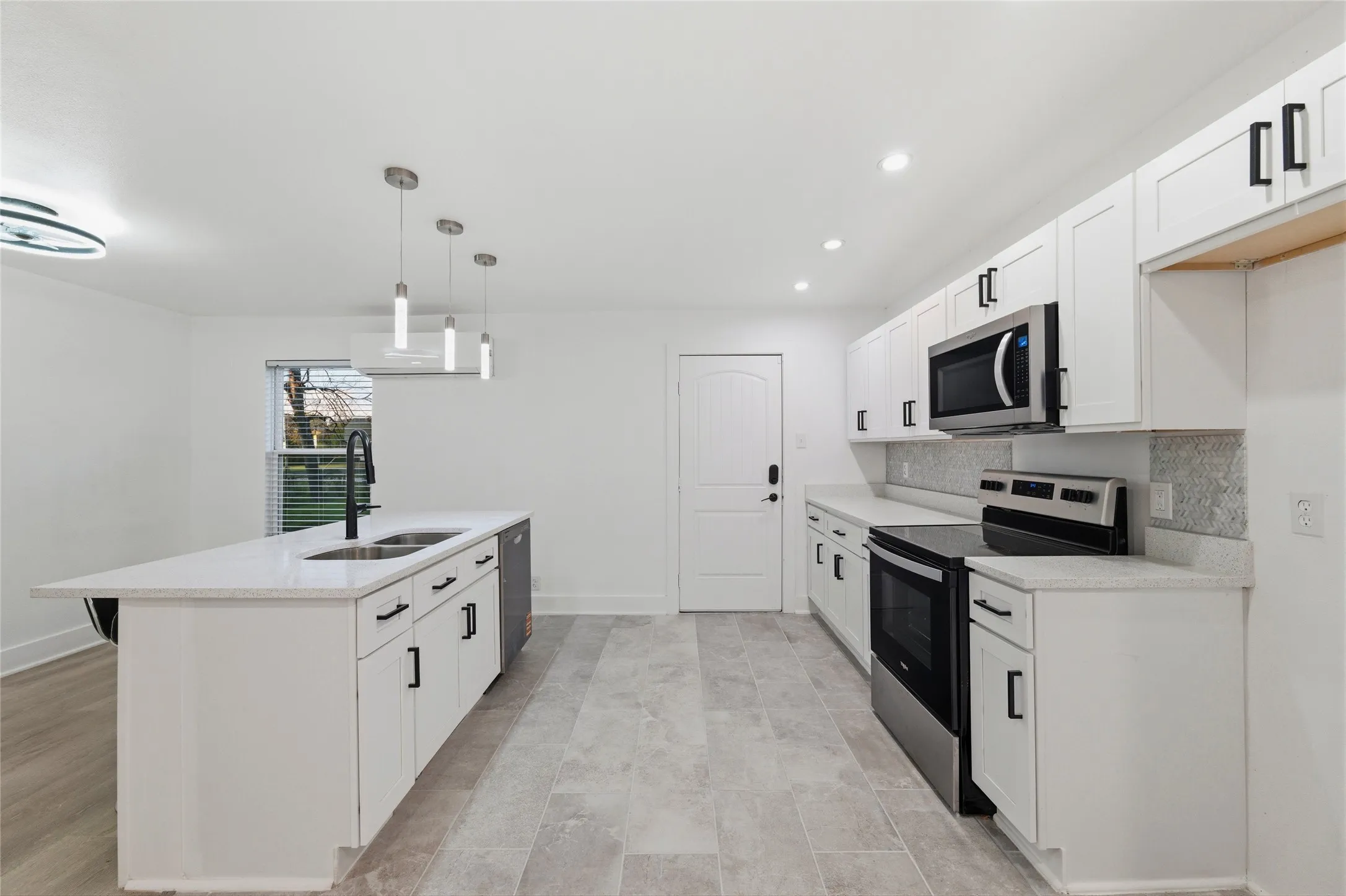 Kitchen featuring stainless steel appliances, white cabinets, a center island with sink, decorative backsplash, and light stone counters
