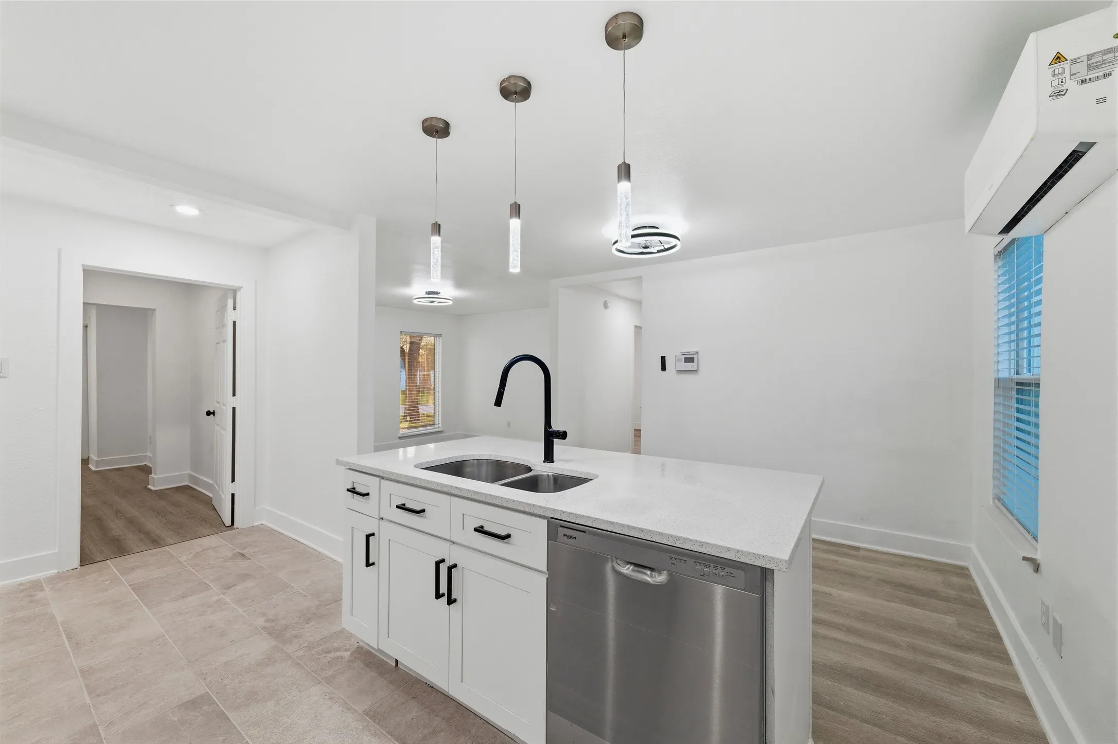 Kitchen featuring stainless steel dishwasher, pendant lighting, an island with sink, light stone countertops, and white cabinets