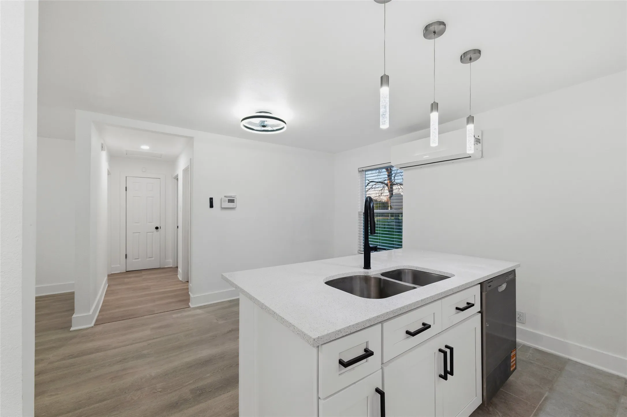 Kitchen with white cabinetry, decorative light fixtures, light stone counters, dishwasher, and a center island with sink