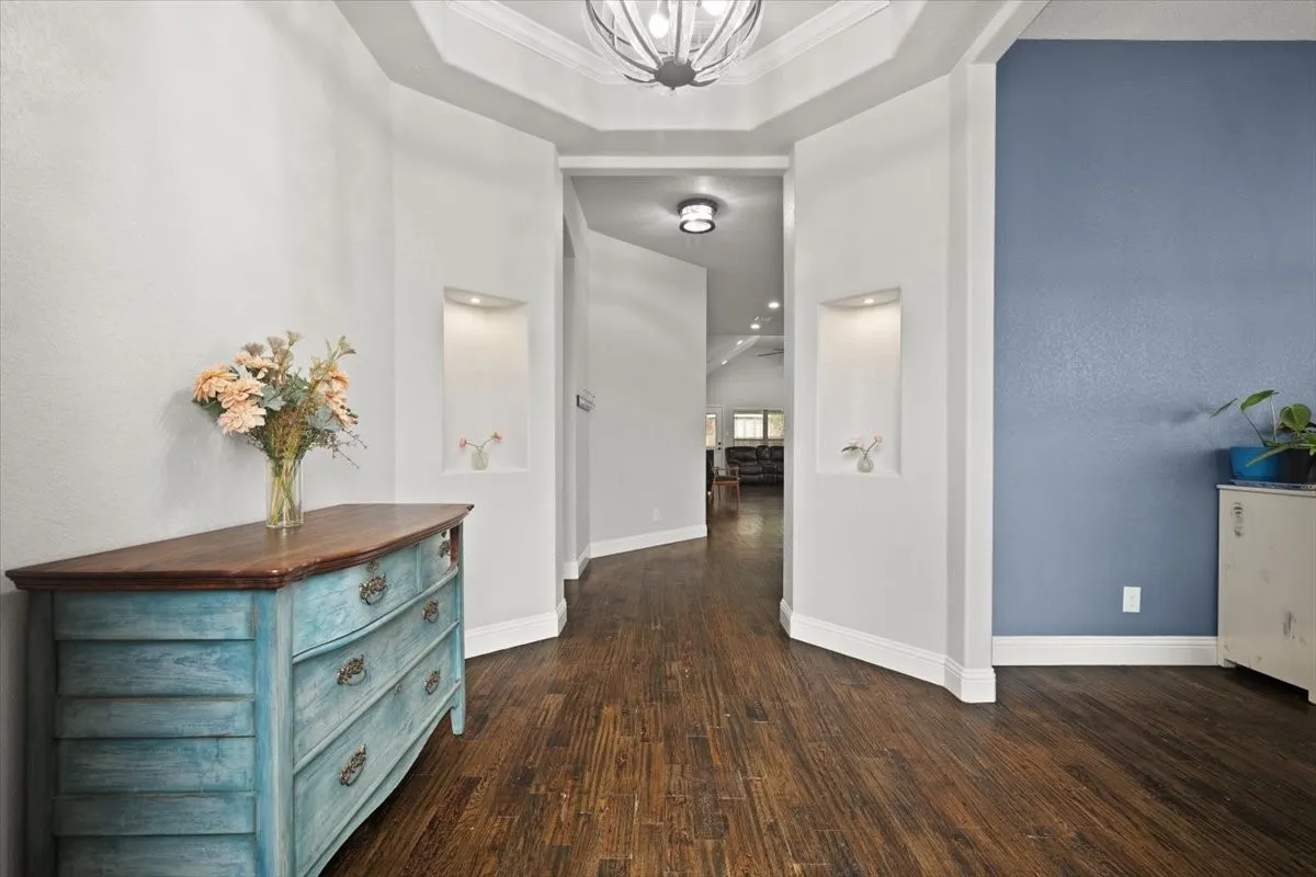 Hall with dark wood-style floors, a chandelier, a raised ceiling, and crown molding