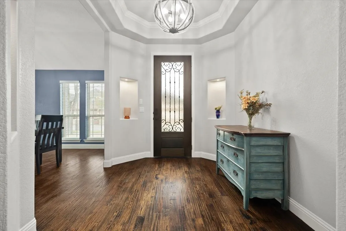 Entrance foyer featuring hanging lights, dark wood-style floors, a textured wall, a tray ceiling, and ornamental molding