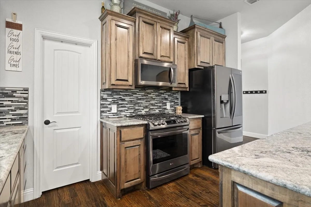Kitchen featuring stainless steel appliances, wood finish cabinetry, dark wood-type flooring, and light stone counters