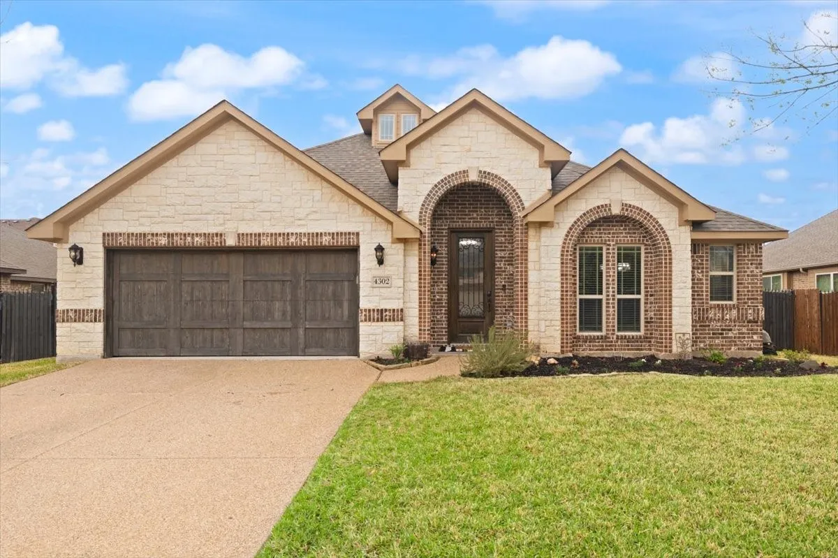 French country style house with stone siding, an attached garage, brick siding, driveway, and a shingled roof