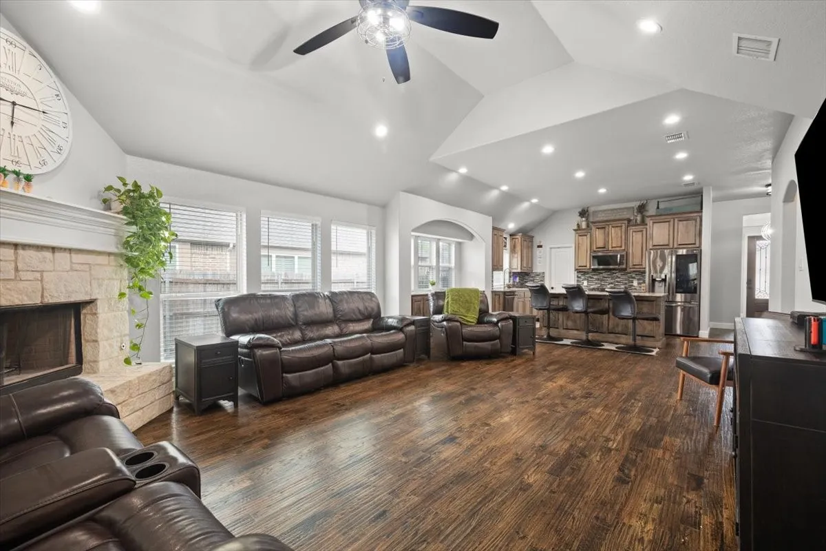 Living area featuring dark wood-style flooring, vaulted ceiling, recessed lighting, ceiling fan, and a fireplace