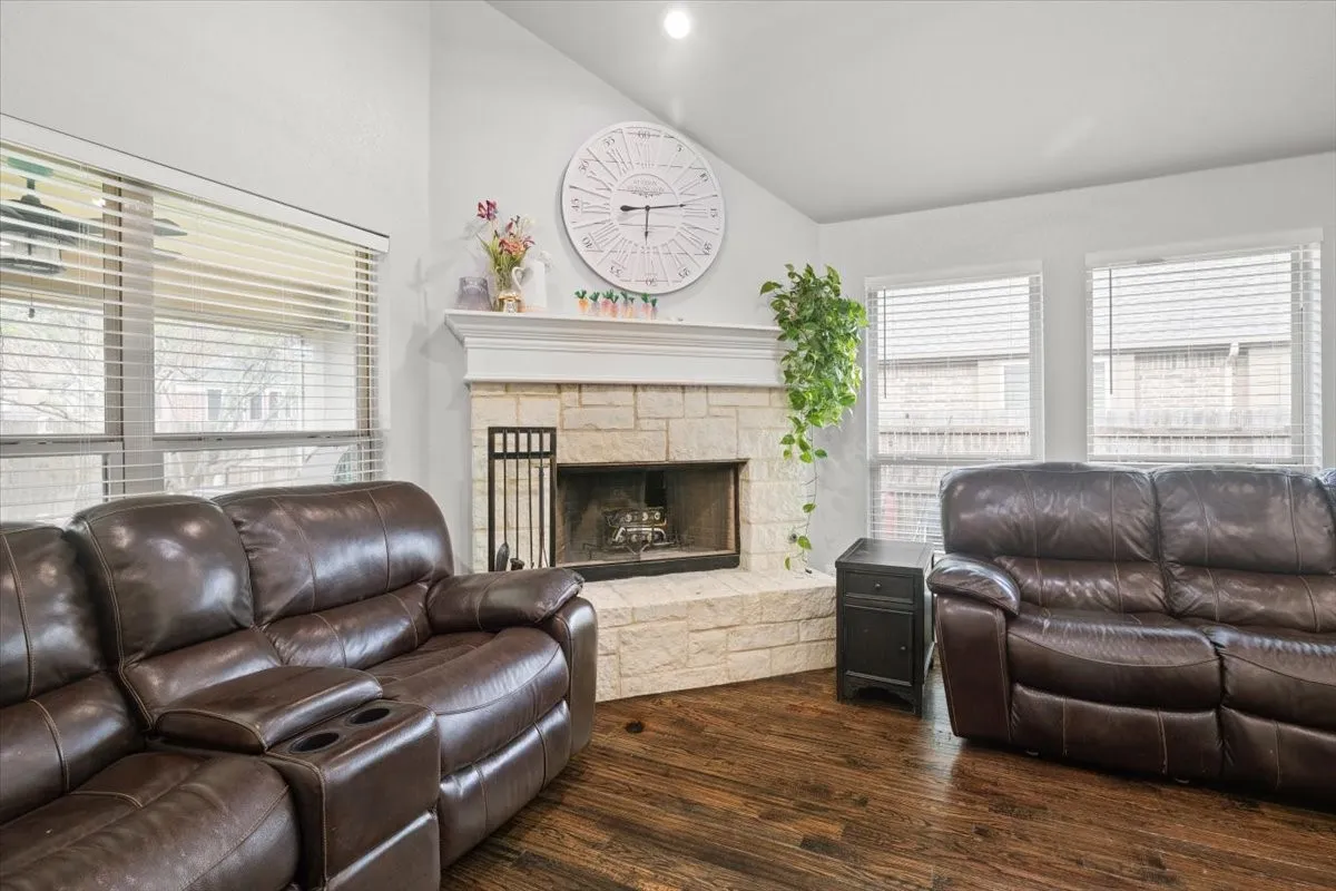 Living area with vaulted ceiling, dark wood-style flooring, a stone fireplace, and recessed lighting