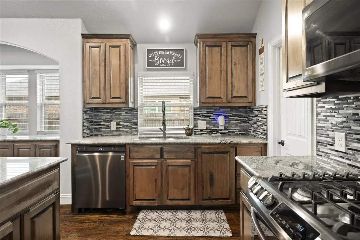 Kitchen featuring stainless steel appliances, decorative backsplash, dark wood finished floors, light stone countertops, and arched walkways