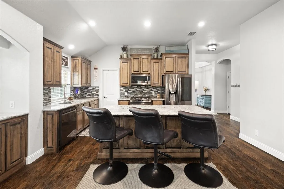 Kitchen featuring arched walkways, a kitchen breakfast bar, stainless steel appliances, a kitchen island, and dark wood-style floors
