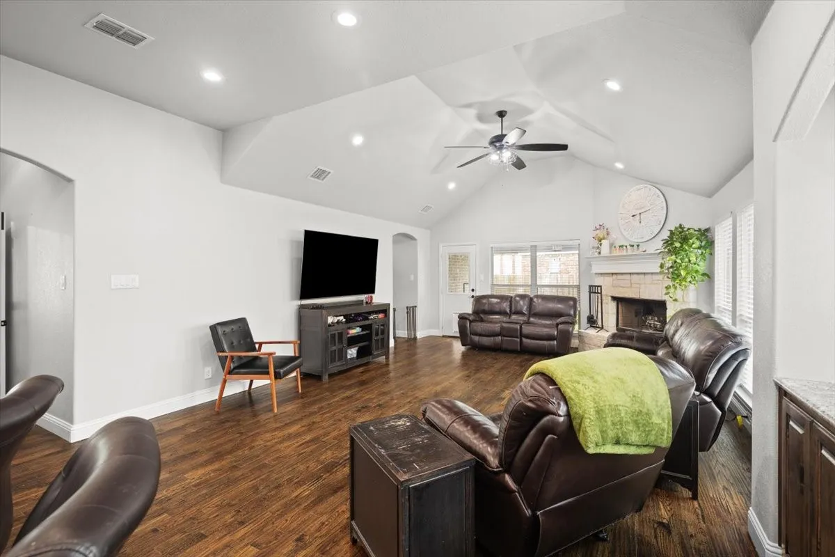 Living room with arched walkways, a fireplace, dark wood finished floors, a high ceiling, and a ceiling fan
