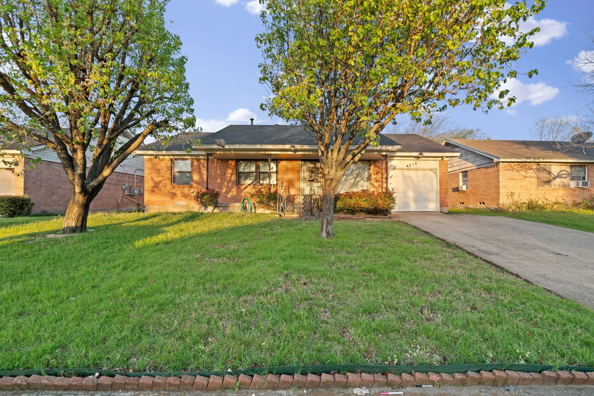Single story home with concrete driveway, brick siding, a front lawn, and an attached garage