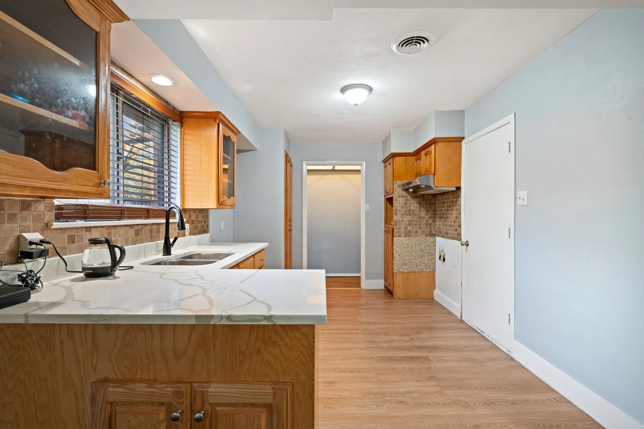 Kitchen featuring glass fronted cabinets, decorative backsplash, light wood-style flooring, and wood finish cabinetry
