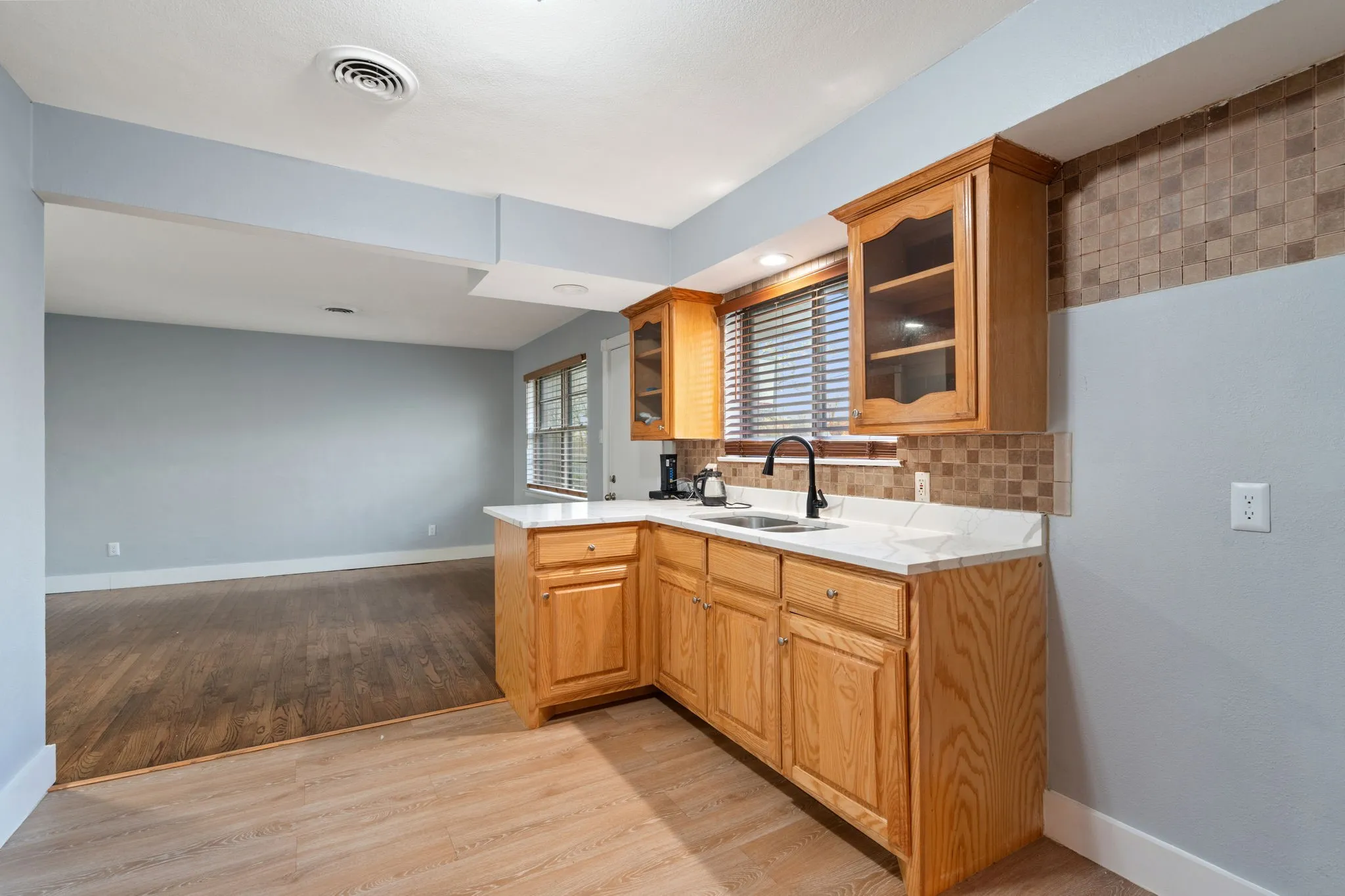 Kitchen with glass insert cabinets, light countertops, a peninsula, light wood-style flooring, and decorative backsplash