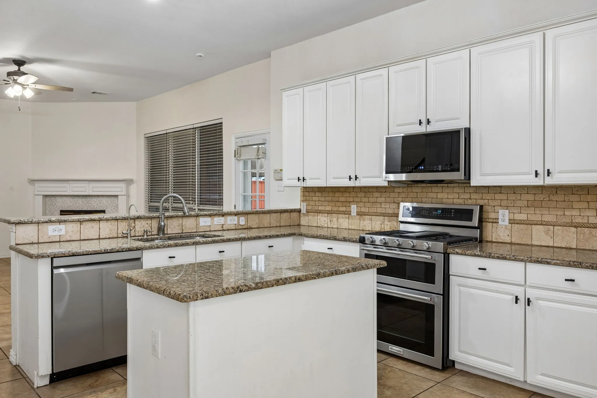 Kitchen featuring granite countertops, white cabinetry, stainless steel appliances, a tile backsplash, and a central island
