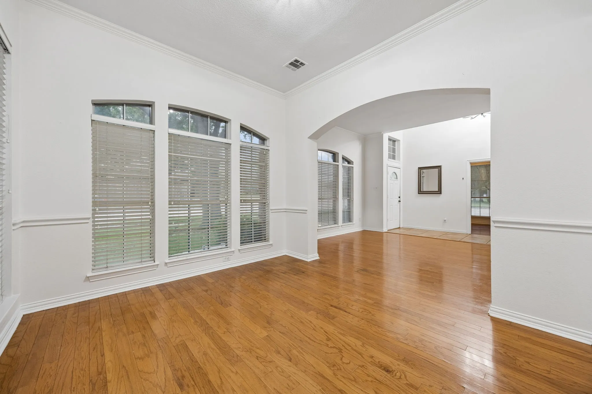 Open-concept room featuring wood-finish flooring, white walls, and bright crown molding
