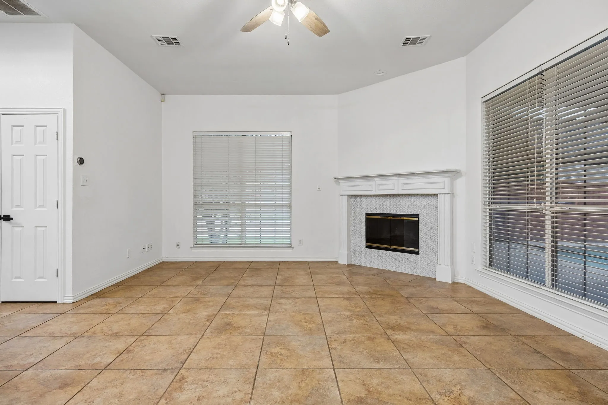 Spacious interior room featuring warm-toned tile flooring, white walls, and a corner fireplace with a decorative mantel and mosaic tile surround
