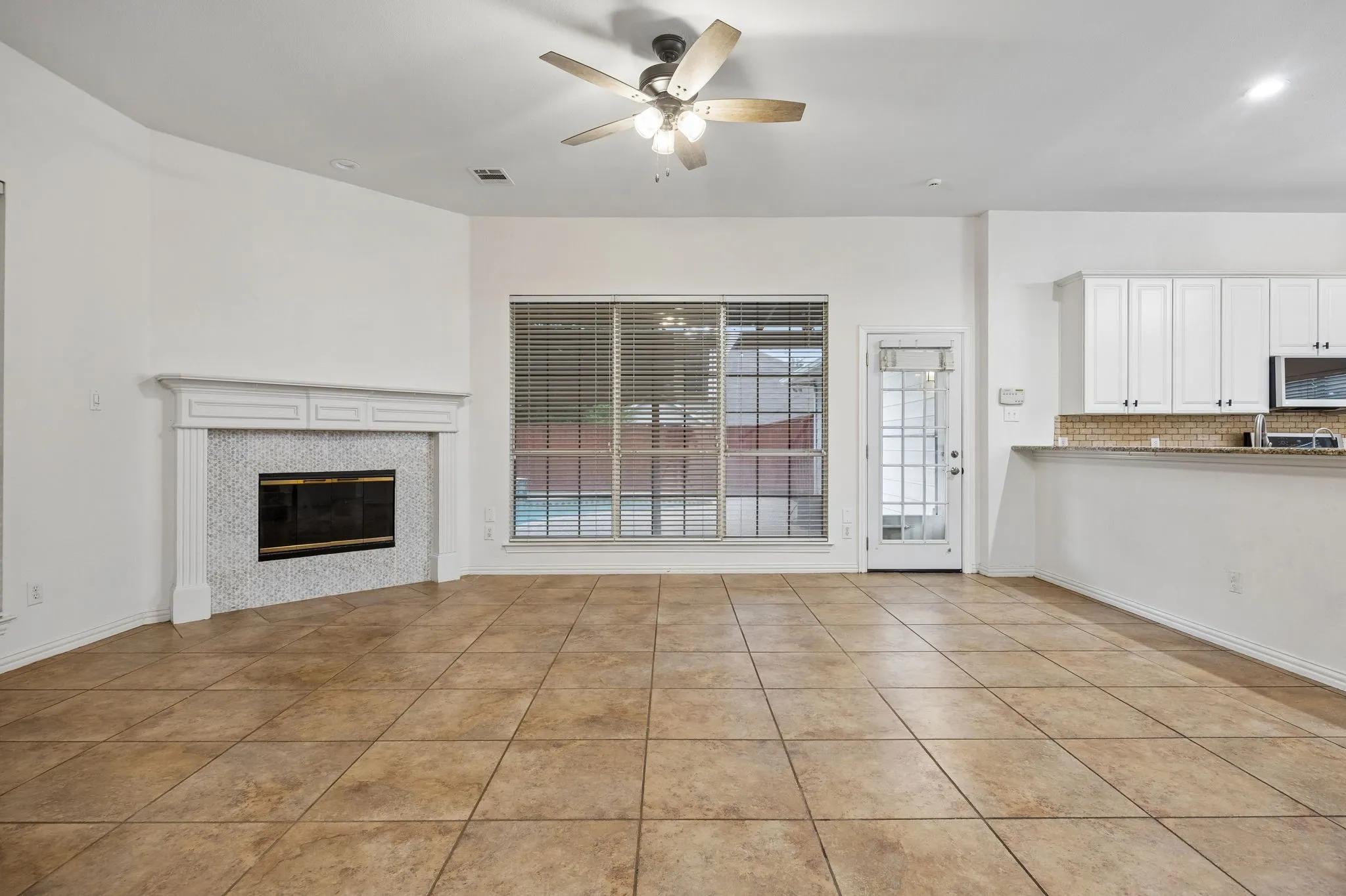 Open-concept living space featuring large format tile flooring, a decorative fireplace with a mosaic tile surround, and expansive windows