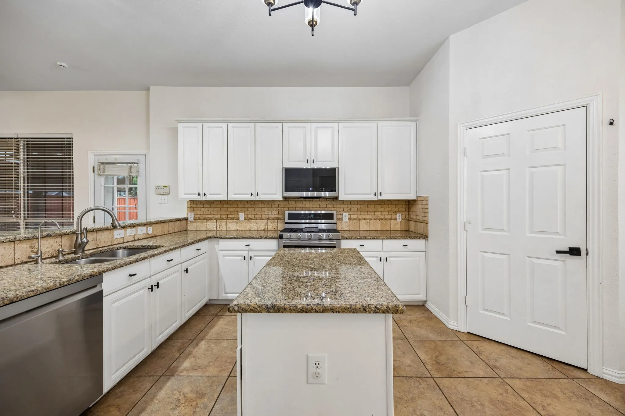 Kitchen featuring white cabinetry, granite countertops, tile flooring, and a central island