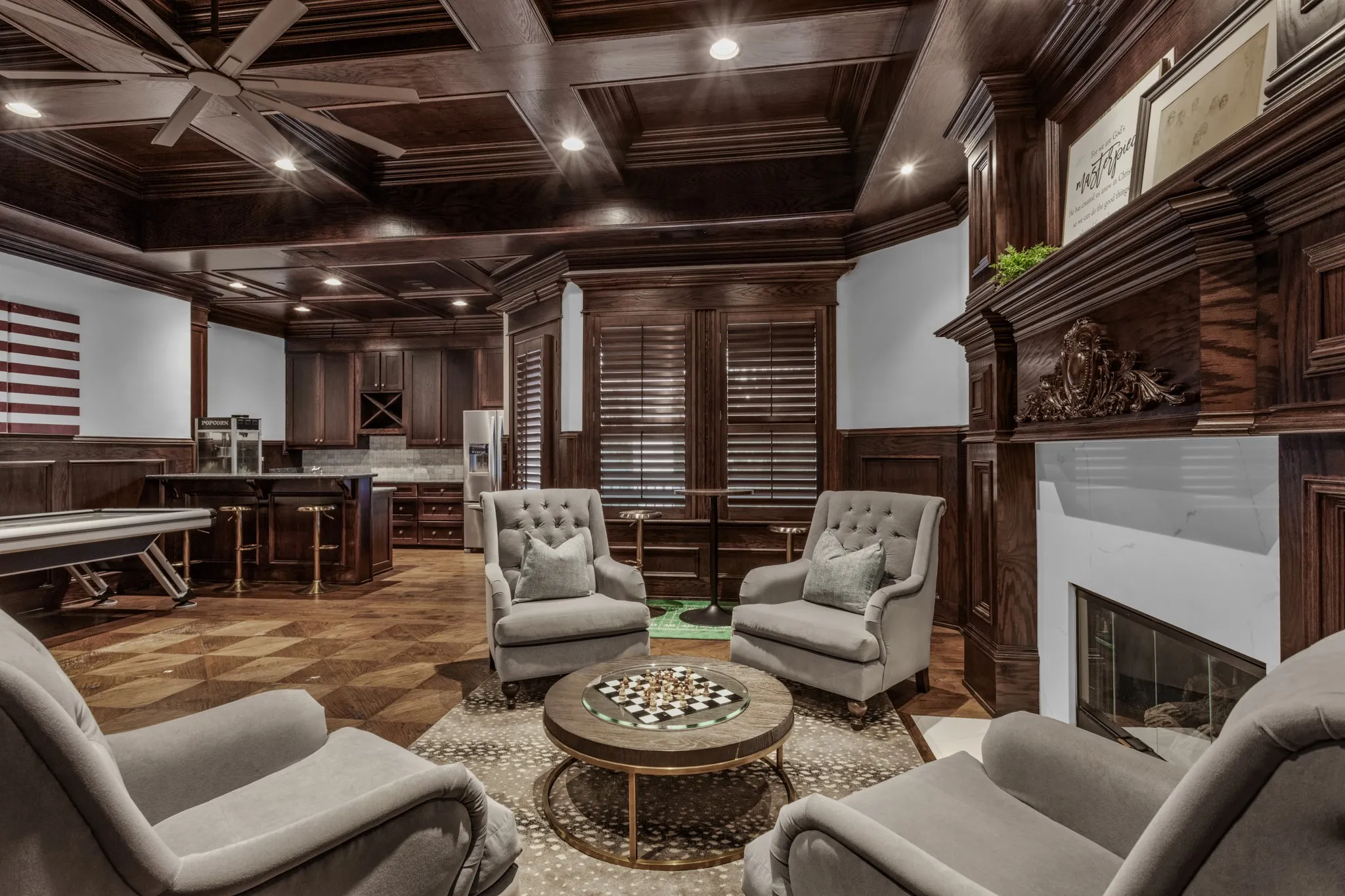 Custom wood-paneled entertainment room featuring a coffered ceiling with recessed lighting, a built-in wet bar, a fireplace with an ornate mantel, and wood-finish flooring