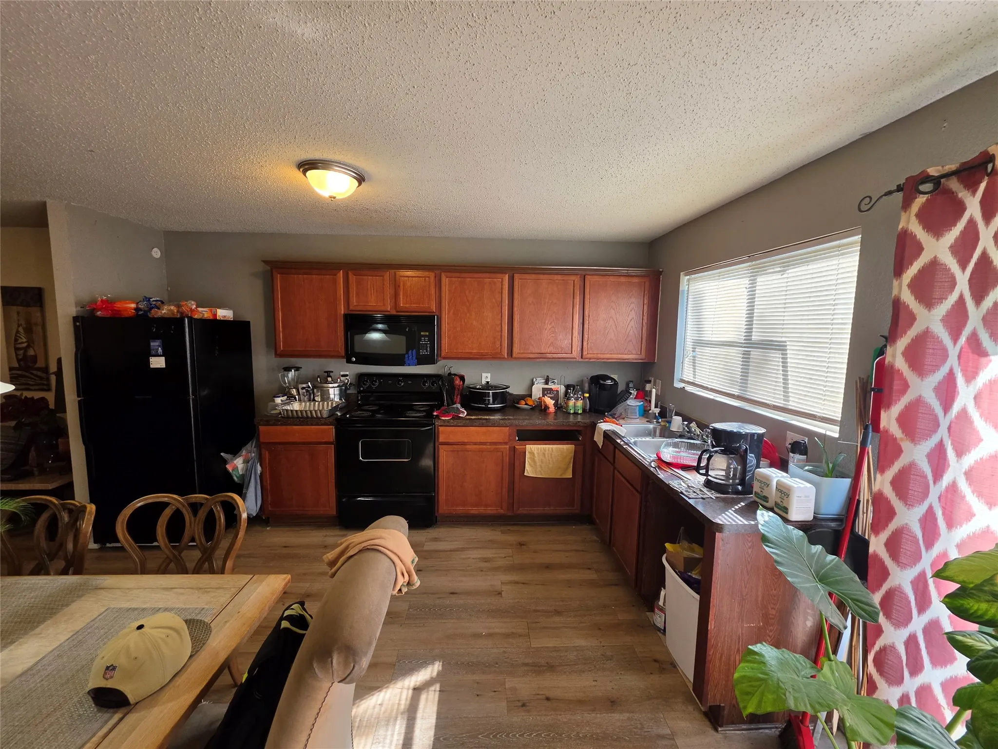 Kitchen with black appliances, wood finish cabinetry, a textured ceiling, dark wood-style flooring, and dark countertops