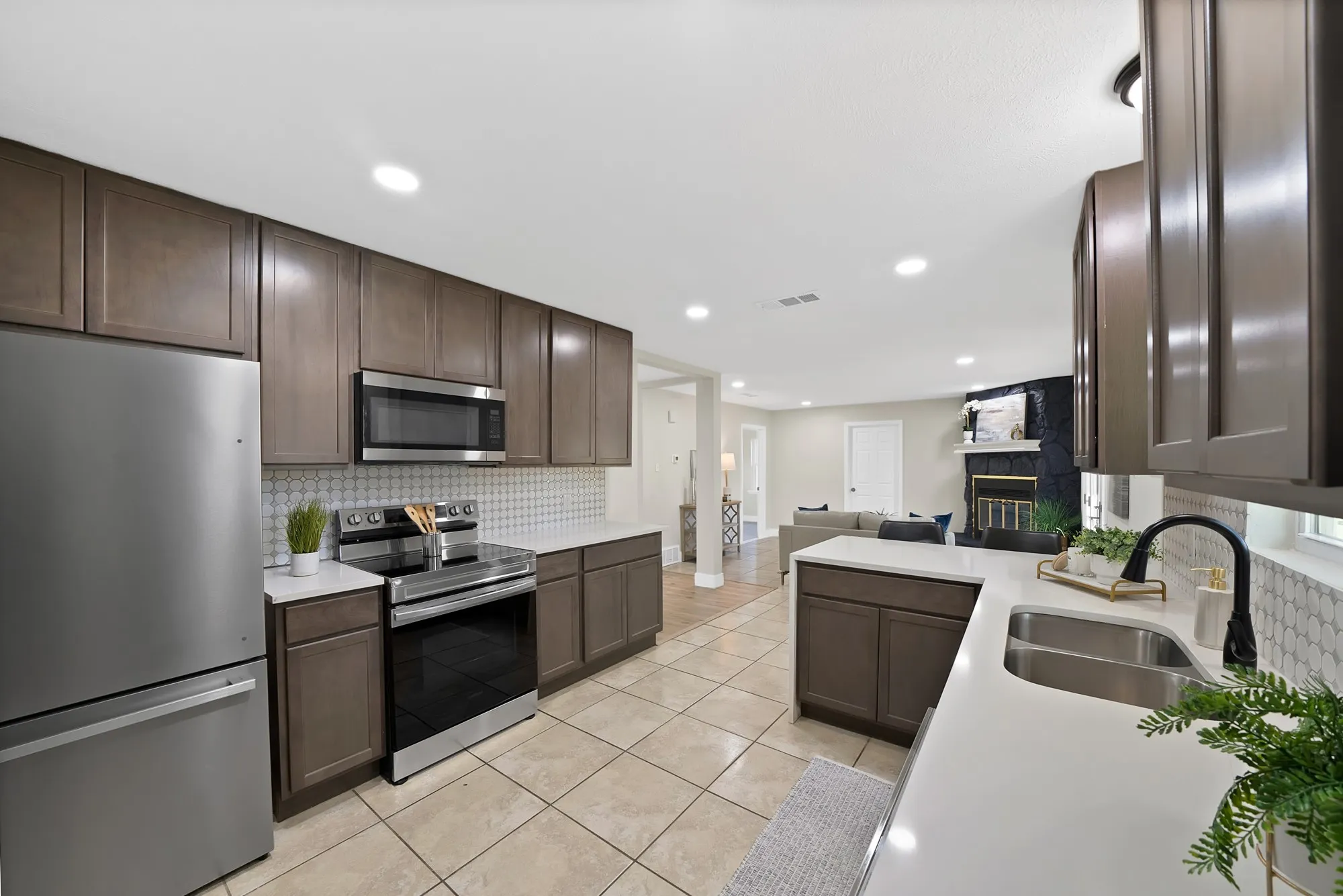 Kitchen with stainless steel appliances, dark wood finish cabinetry, open floor plan, a glass covered fireplace, and light tile patterned flooring
