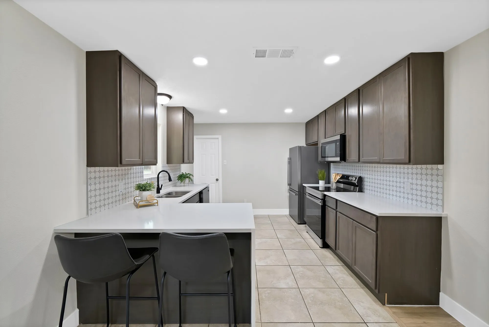 Kitchen featuring dark wood finish cabinets, stainless steel appliances, a kitchen bar, tasteful backsplash, and light tile patterned flooring