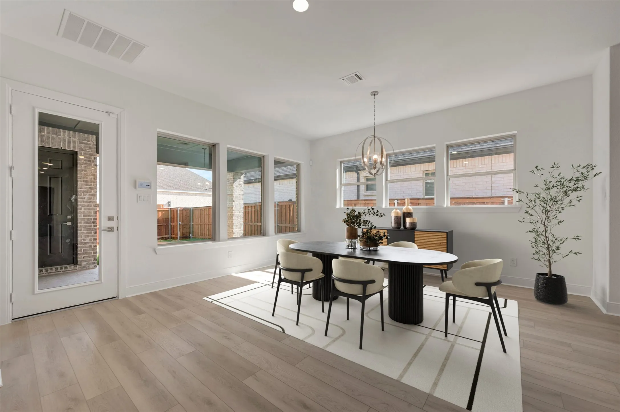 Open-concept dining area featuring wood-finish flooring, a contemporary chandelier, and multiple windows