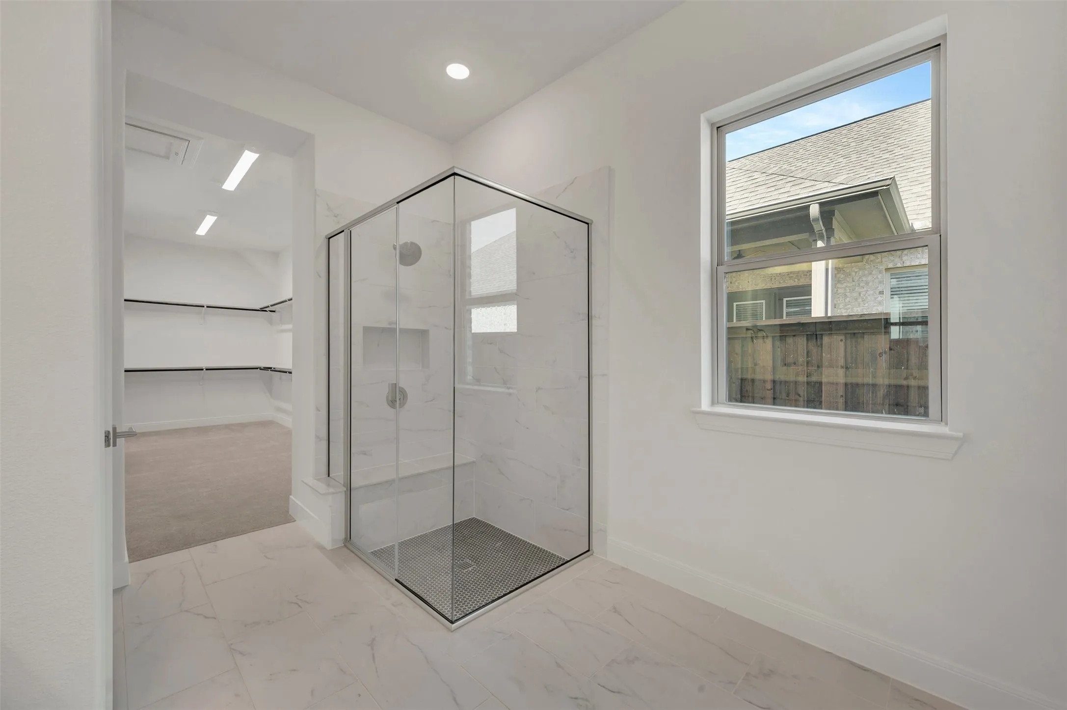 Glass-enclosed shower with white marble-style tile surround and integrated niche