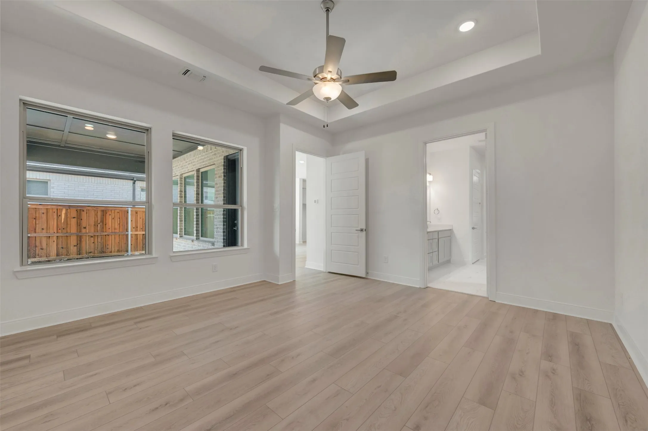 Spacious room featuring light wood-finish flooring, a tray ceiling with a ceiling fan, and recessed lighting