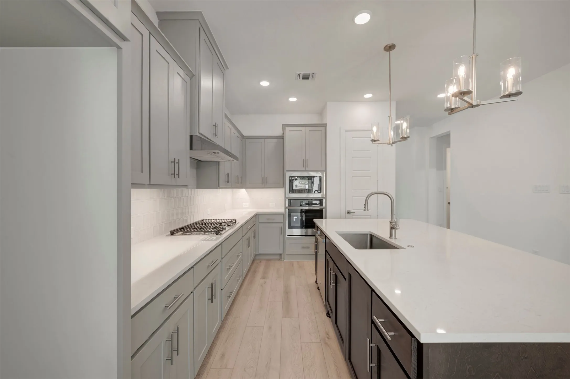 Contemporary kitchen featuring an expansive island with an undermount sink, light-toned countertops, gray cabinetry, and stainless steel appliances